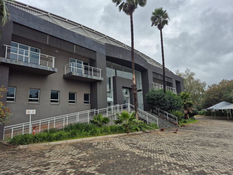 Modern industrial office building exterior featuring a dark facade, glass entrance, paved driveway, and multiple balconies with metal railings.