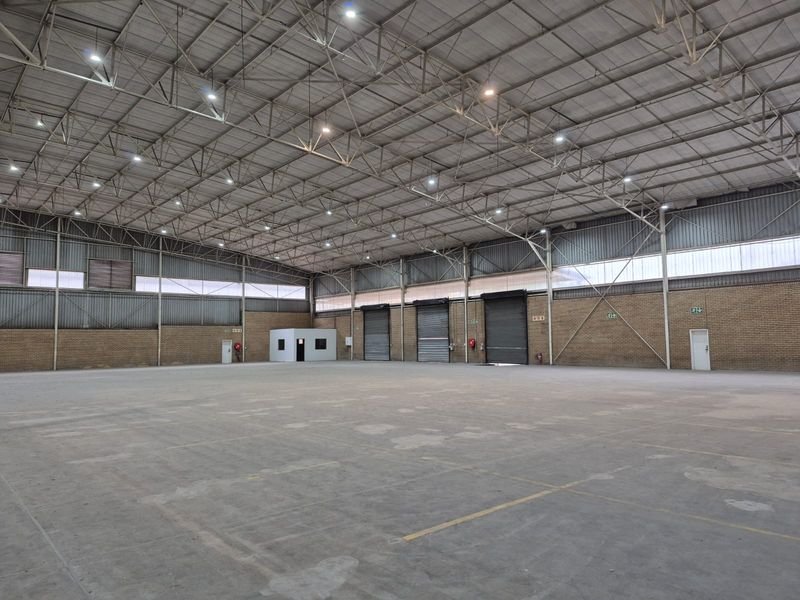 Spacious industrial warehouse featuring high ceilings with steel truss construction, multiple roller shutter doors, concrete flooring, and an integrated internal office structure.