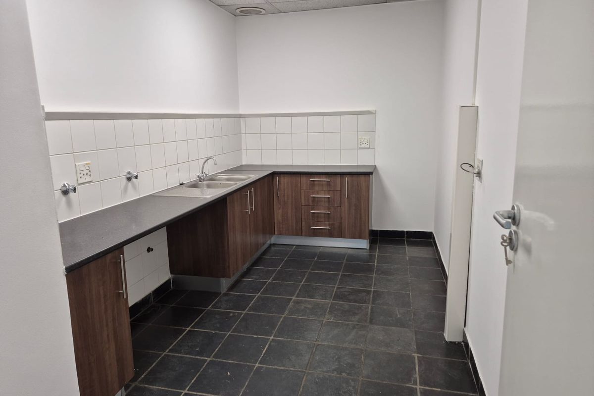 A functional industrial kitchenette featuring dark laminate cabinetry, stone countertops, a stainless steel sink, and durable slate flooring.