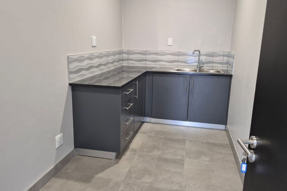 A compact kitchenette featuring modern grey cabinetry, dark stone-look countertops, a stainless steel sink, and decorative wave-patterned backsplash tiling.