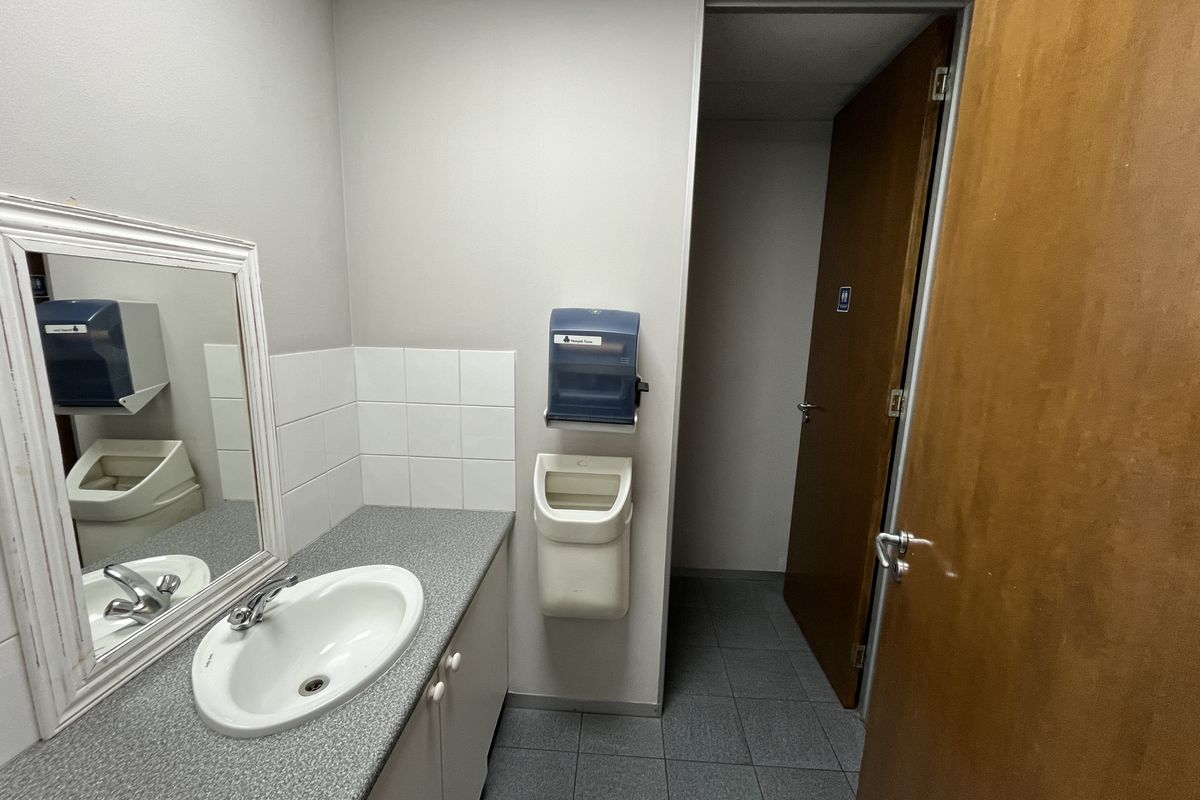 A functional office restroom featuring a built-in vanity with a laminate countertop, integrated sink, and tiled splashback.