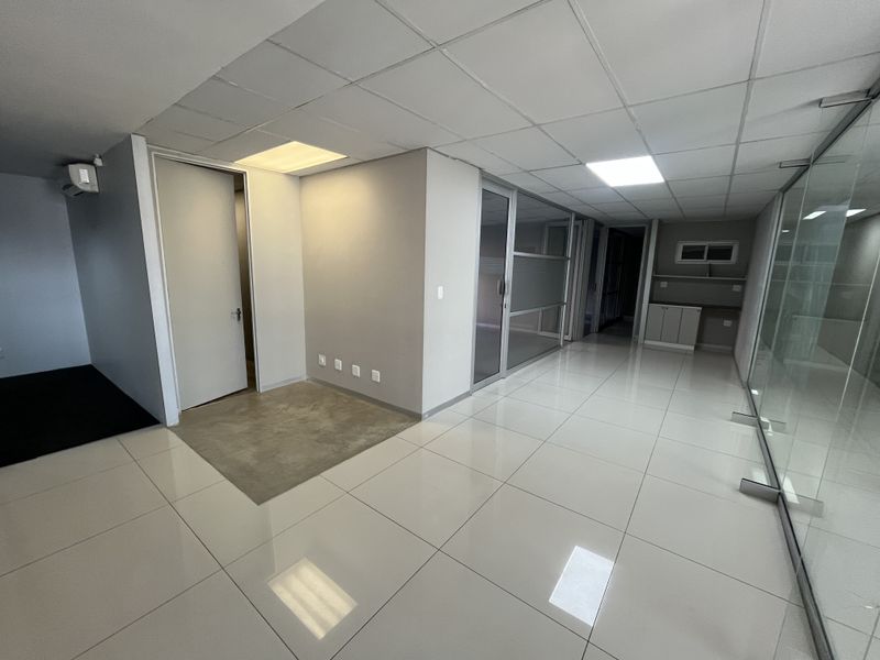 Modern open-plan office space featuring polished tiled flooring, glass partitions, suspended ceilings with recessed lighting, and integrated cabinetry.