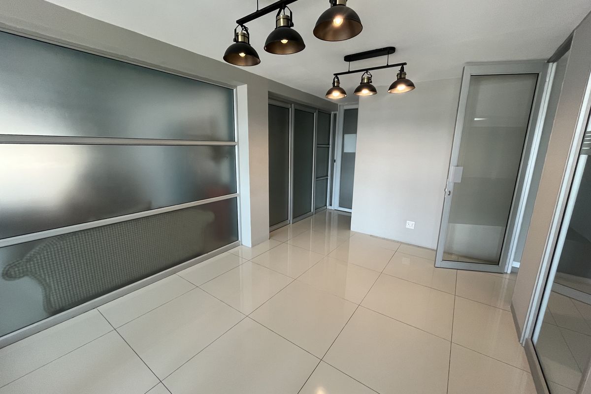 Modern office space featuring polished tile flooring, frosted glass partitions, and contemporary industrial pendant lighting, offering a clean and professional environment.