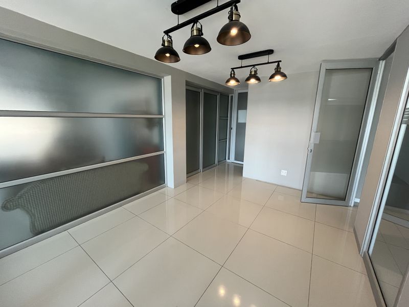 Modern office space featuring polished tile flooring, frosted glass partitions, and contemporary industrial pendant lighting, offering a clean and professional environment.