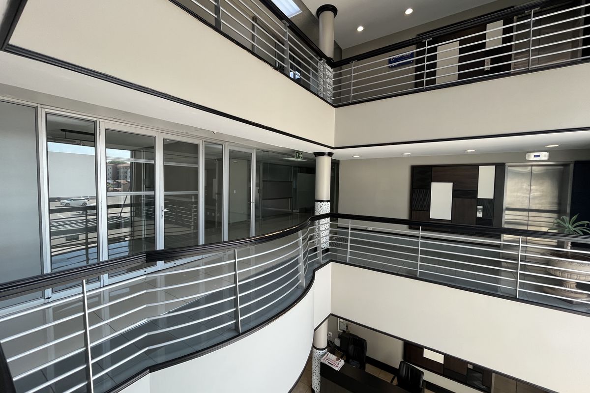 A modern multi-level commercial office atrium featuring tiled floors, stainless steel balustrades, glass partitions, and an elevator, providing a professional and open circulation space.