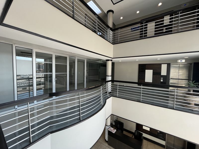A modern multi-level commercial office atrium featuring tiled floors, stainless steel balustrades, glass partitions, and an elevator, providing a professional and open circulation space.