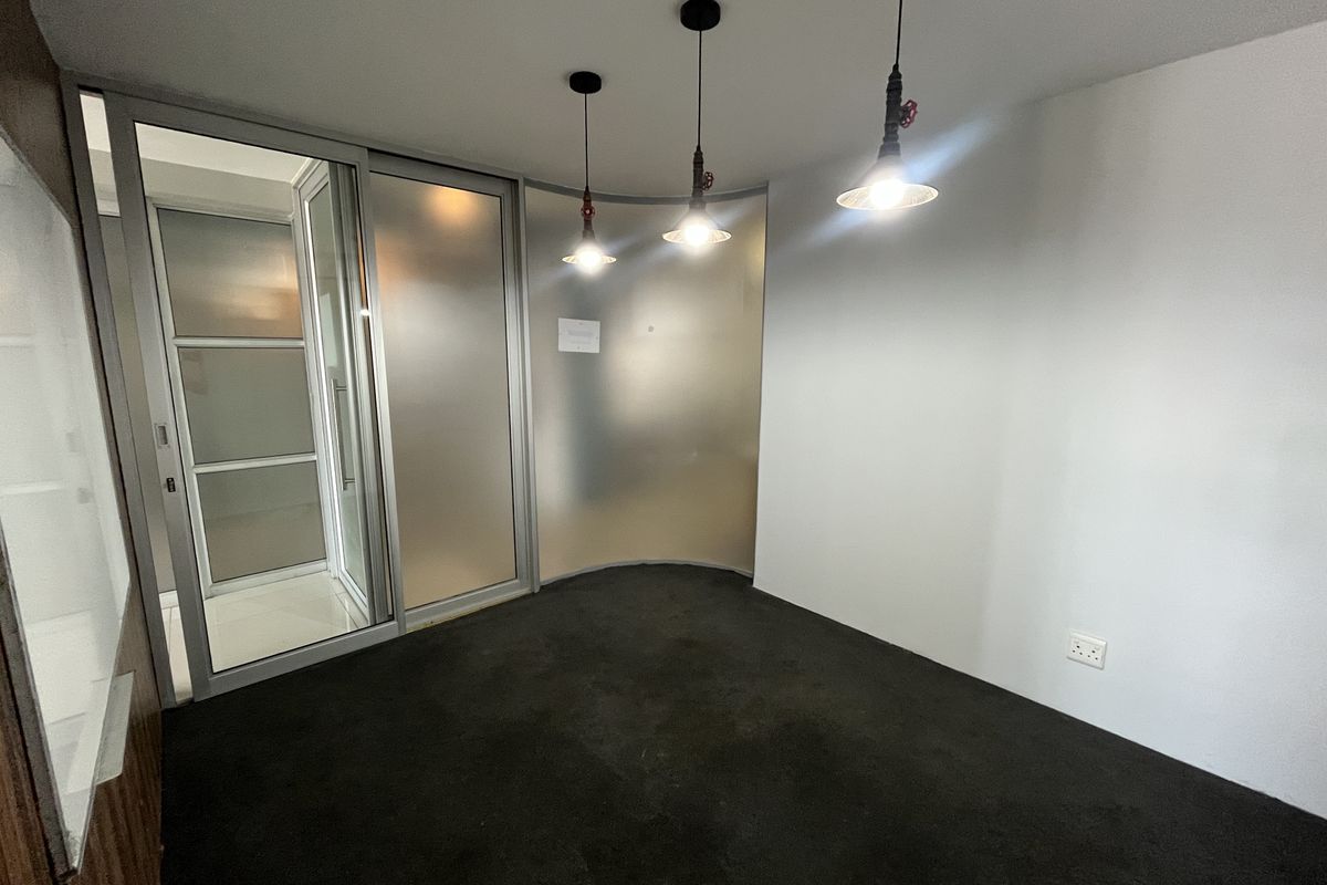 A clean, empty office space featuring a curved frosted glass partition, sliding glass entry door, and modern industrial-style pendant lighting.