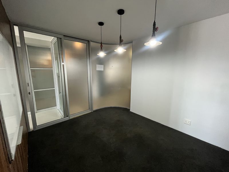 A clean, empty office space featuring a curved frosted glass partition, sliding glass entry door, and modern industrial-style pendant lighting.