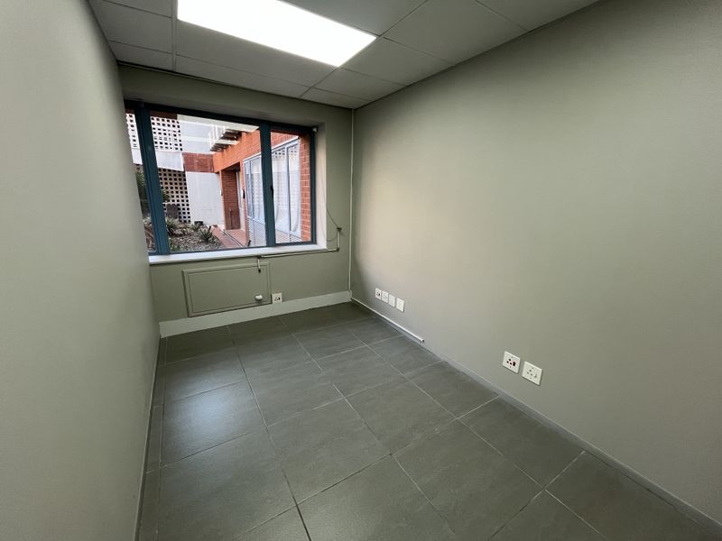 A clean, empty office space featuring tiled flooring, a drop ceiling with recessed lighting, and multiple electrical power points, suitable for a professional workspace.