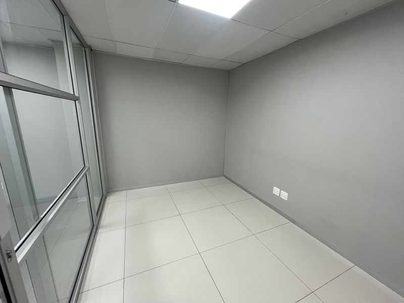 A clean, empty office space featuring modern tiled flooring, a suspended ceiling, and a glass partition wall, ready for professional use.