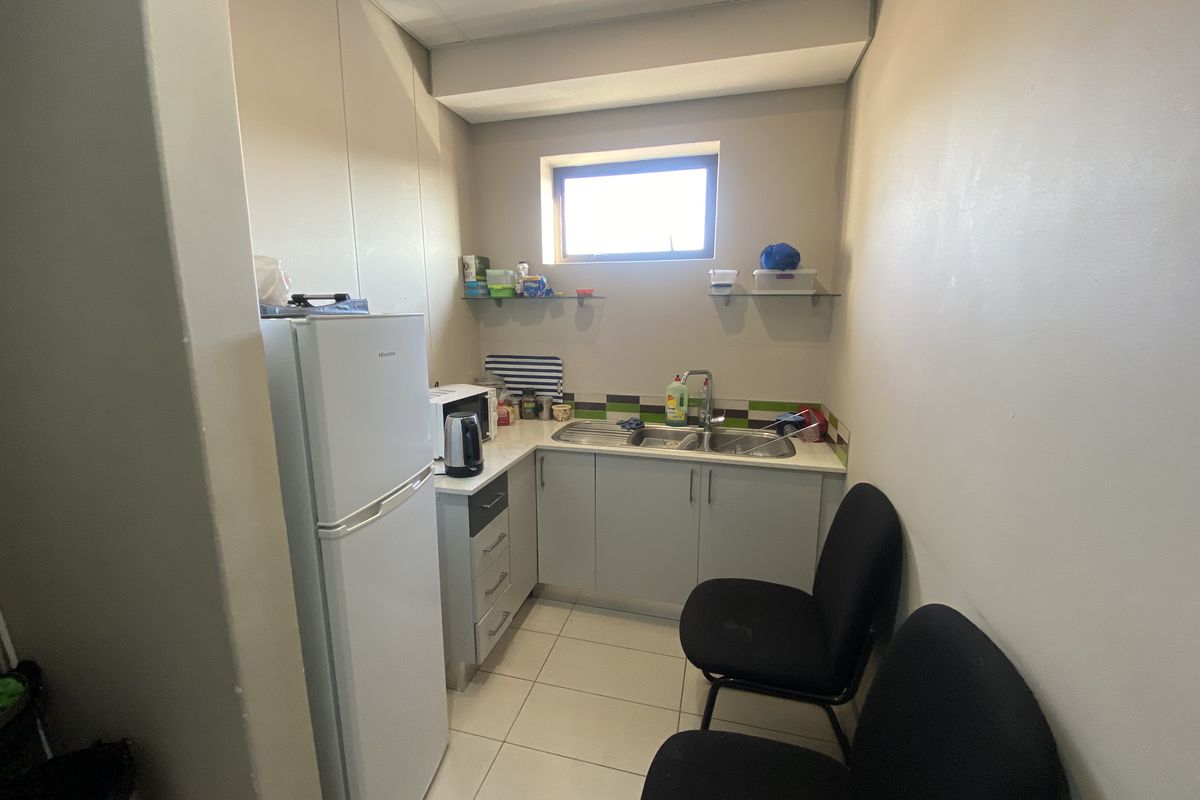 A compact office kitchenette featuring built-in cabinetry, a stainless steel sink, tiled flooring, and a small window for natural light.