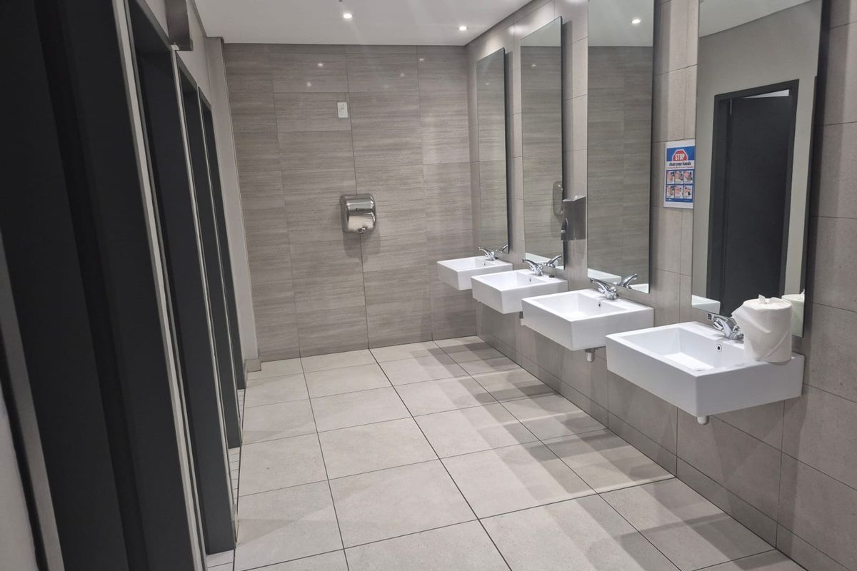 Modern industrial restroom facility featuring multiple wall-mounted ceramic basins, large vanity mirrors, and tiled wall and floor finishes.