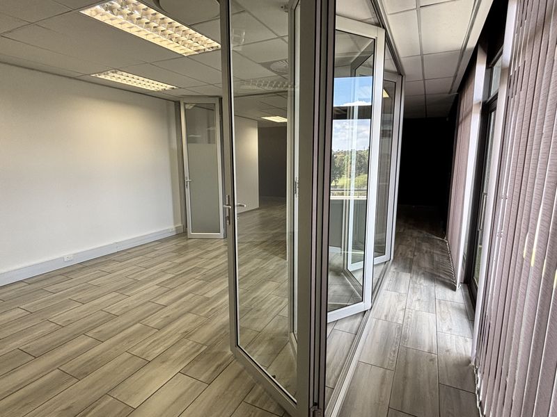 Modern open-plan office space featuring wood-look tile flooring, suspended ceilings with recessed lighting, and glass partition doors for a bright, professional environment.