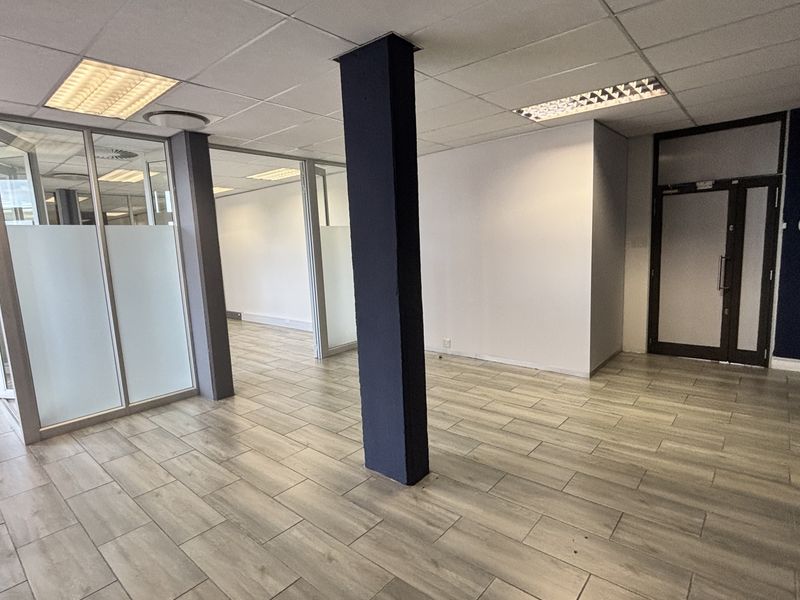 A modern, open-plan office space featuring wood-look tile flooring, glass partitions, and a neutral color palette, ideal for a professional workspace.