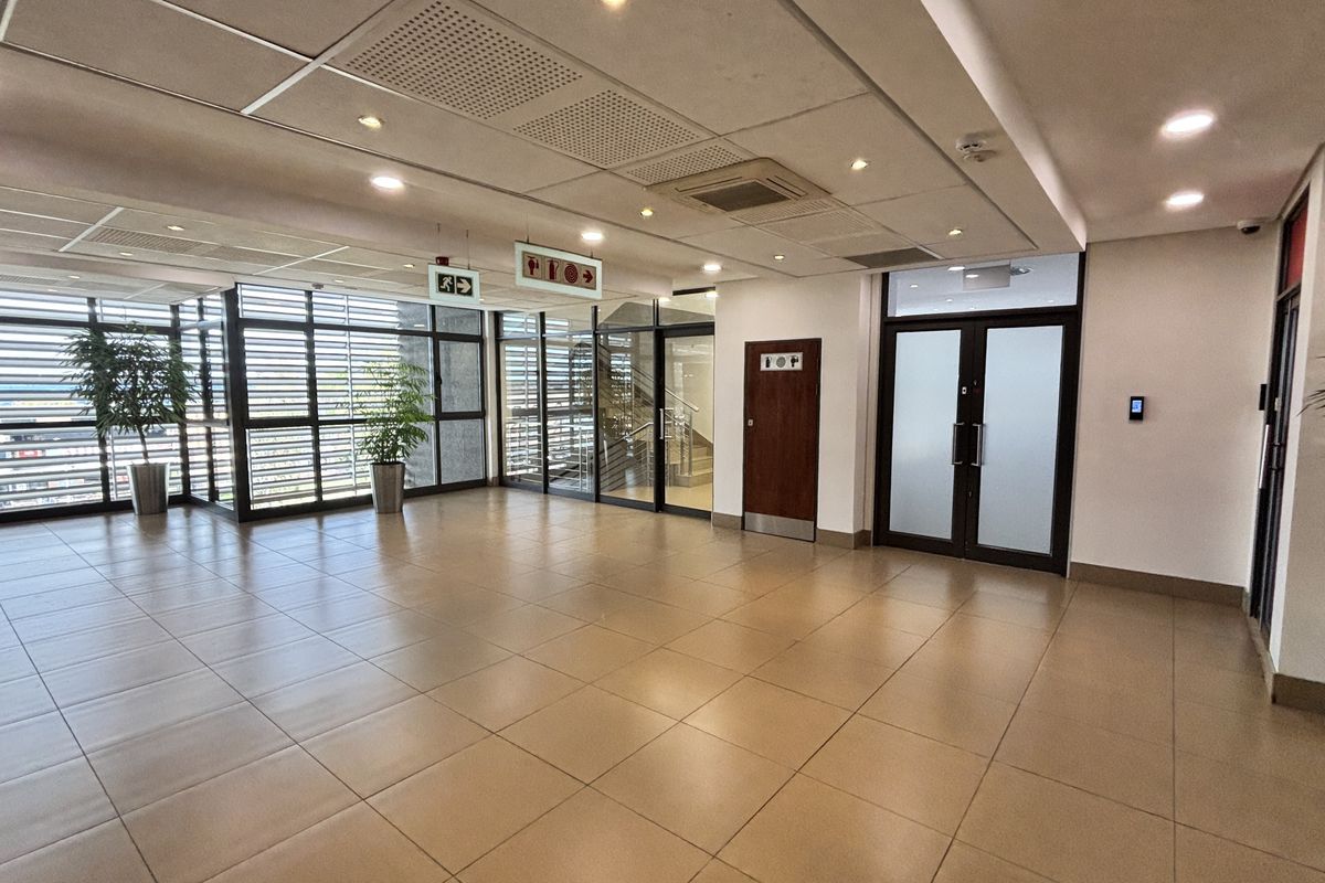 A spacious, modern office lobby or reception area featuring tiled flooring, suspended ceilings with recessed lighting, and glass partition walls.