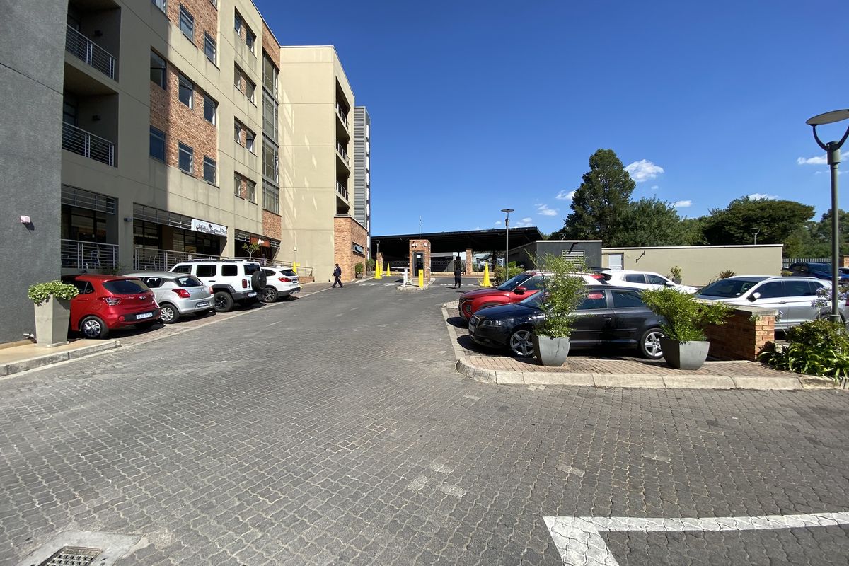 A view of the office complex entrance featuring a paved parking area, multi-story building facade, and a security access gatehouse.