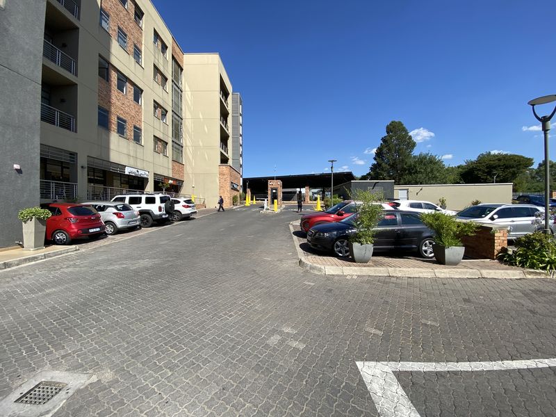 A view of the office complex entrance featuring a paved parking area, multi-story building facade, and a security access gatehouse.