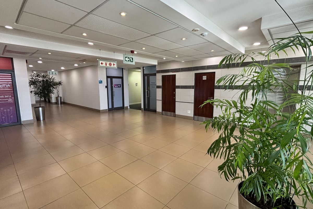 A spacious, well-maintained commercial office hallway featuring neutral ceramic floor tiles, a suspended ceiling with recessed lighting, and multiple access doors.