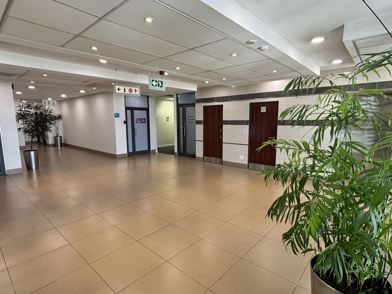 A spacious, well-maintained commercial office hallway featuring neutral ceramic floor tiles, a suspended ceiling with recessed lighting, and multiple access doors.