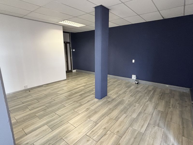 A clean, vacant office space featuring modern wood-look tile flooring, a central structural column, and a suspended ceiling with recessed lighting.