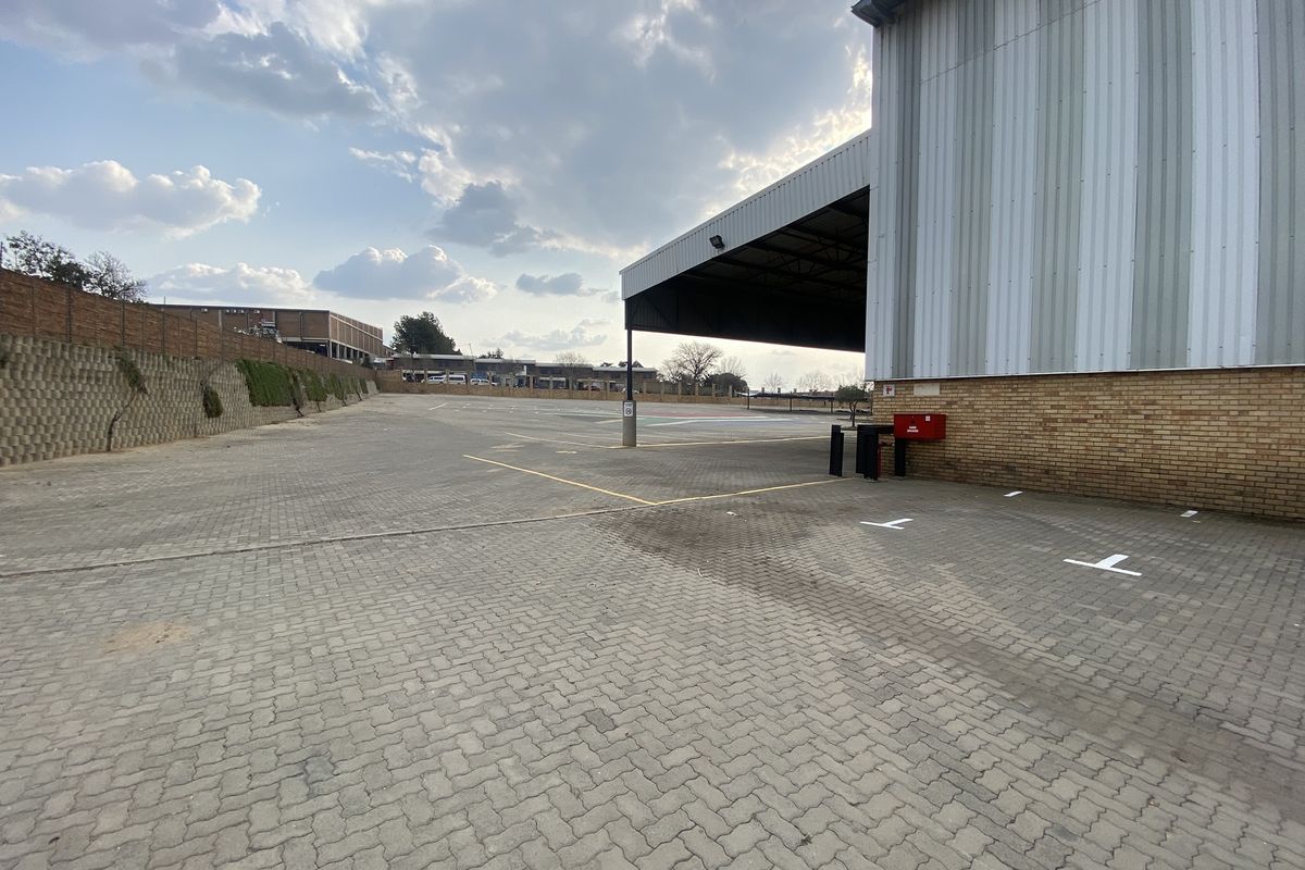 Spacious industrial exterior yard featuring paved parking area, retaining wall, and a large covered loading bay attached to the main warehouse structure.