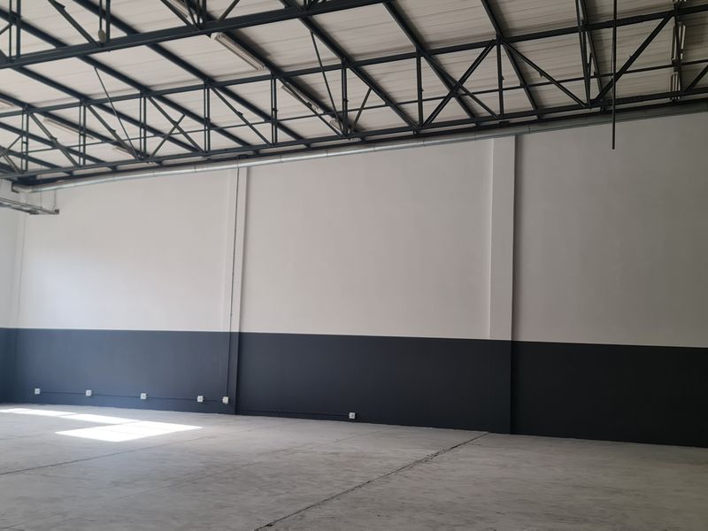 Spacious industrial warehouse unit featuring high exposed steel roof trusses, polished concrete flooring, and large windows providing ample natural light.