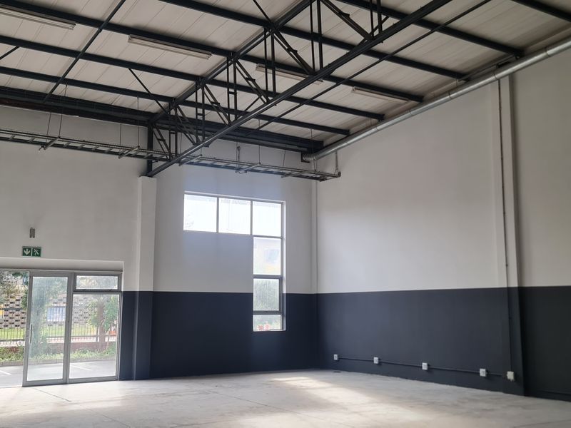 Spacious industrial utility space featuring high ceilings with exposed steel trusses, concrete flooring, and large aluminum-framed windows and doors providing ample natural light.