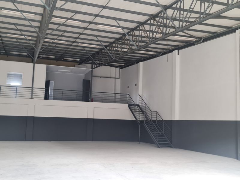 Spacious industrial warehouse unit featuring high ceilings with exposed steel trusses, a mezzanine level with staircase access, and durable concrete flooring.