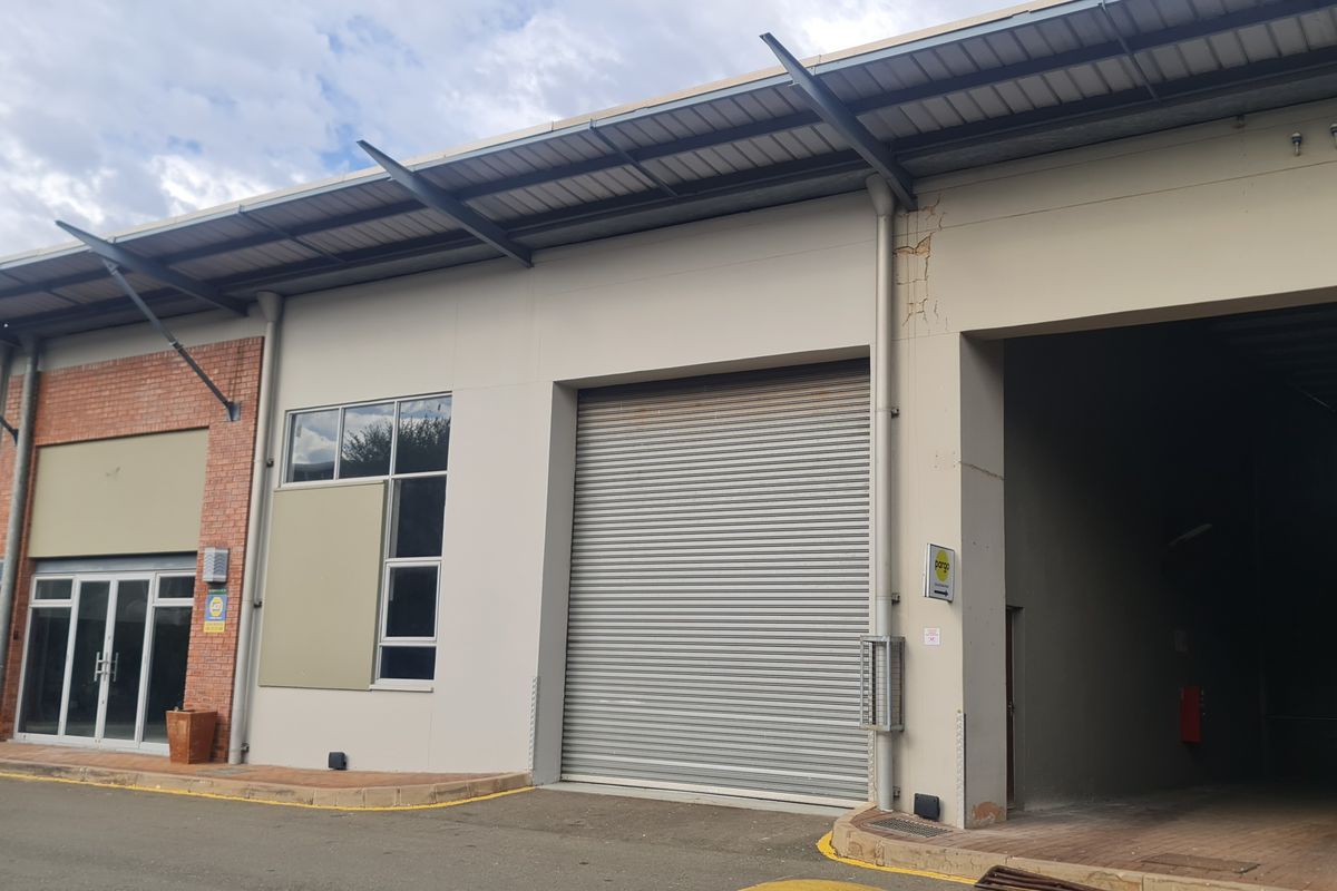 Industrial warehouse unit featuring a large roller shutter door, glass entrance, and covered loading area with brick and plaster facade.