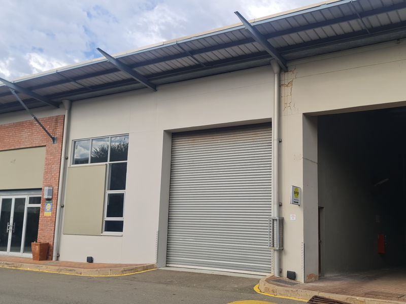 Industrial warehouse unit featuring a large roller shutter door, glass entrance, and covered loading area with brick and plaster facade.