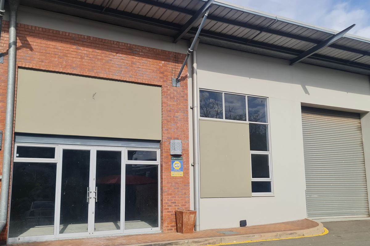 Industrial unit exterior featuring a roller shutter door, glass entrance, and brick facade with metal roofing.