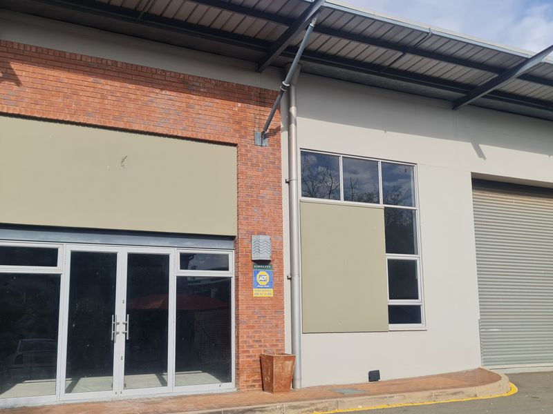 Industrial unit exterior featuring a roller shutter door, glass entrance, and brick facade with metal roofing.
