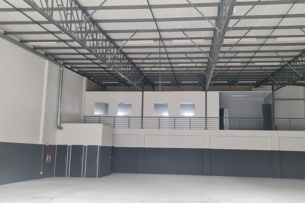 Spacious industrial warehouse unit featuring high ceilings with exposed steel trusses, a mezzanine level with staircase access, and clean, modern finishes.