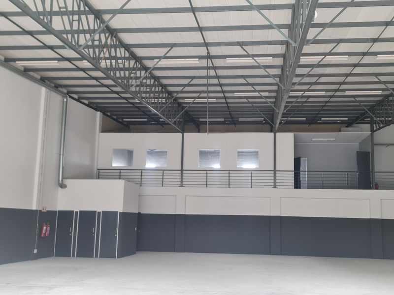 Spacious industrial warehouse unit featuring high ceilings with exposed steel trusses, a mezzanine level with staircase access, and clean, modern finishes.