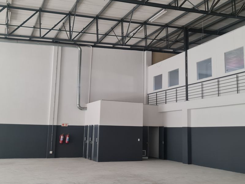 Spacious industrial warehouse unit featuring high ceilings with exposed steel trusses, a mezzanine level with metal railing, and polished concrete flooring.