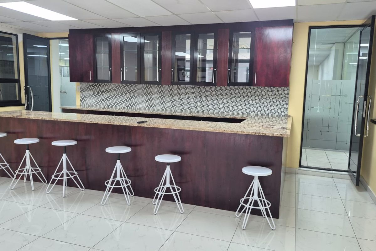 Office breakroom area featuring a large built-in kitchenette with granite countertops, dark wood cabinetry, and a mosaic tile backsplash.