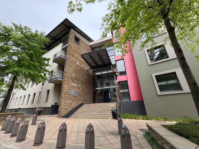 Modern office building entrance featuring stone cladding, a prominent metal canopy, and glass facade with paved pedestrian access.