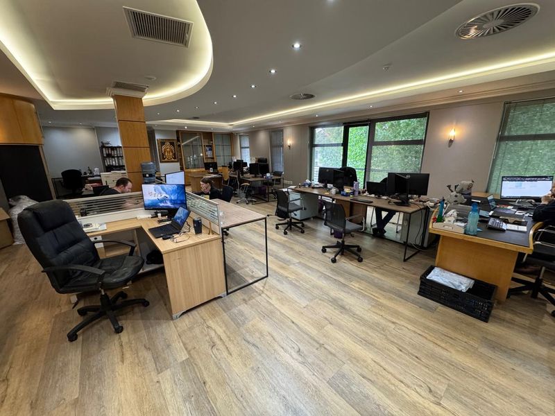 Spacious open-plan office area featuring modern wood-look flooring, recessed cove lighting, and large windows providing ample natural light.