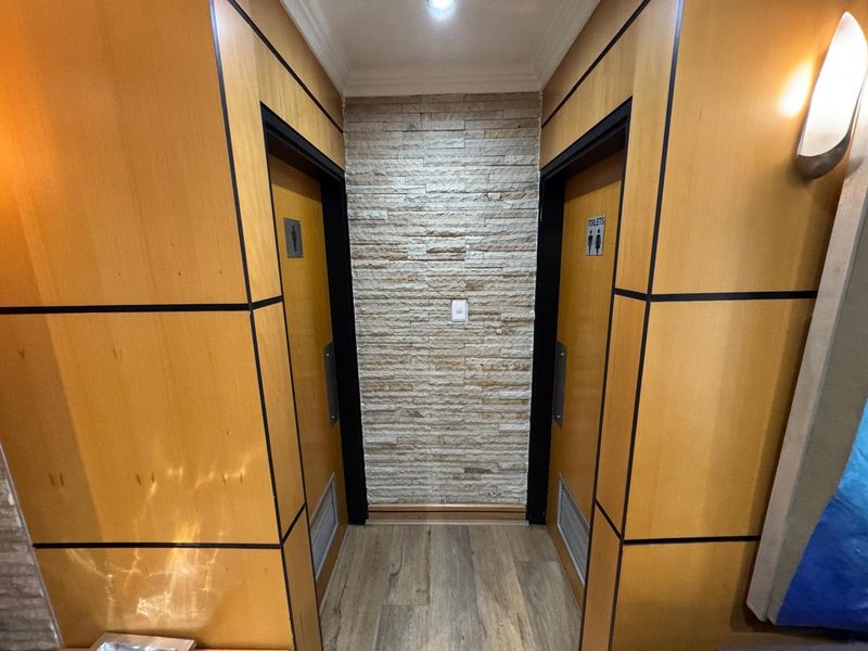 A modern office hallway featuring wood veneer wall paneling, a stacked stone accent wall, and integrated lighting leading to restroom facilities.