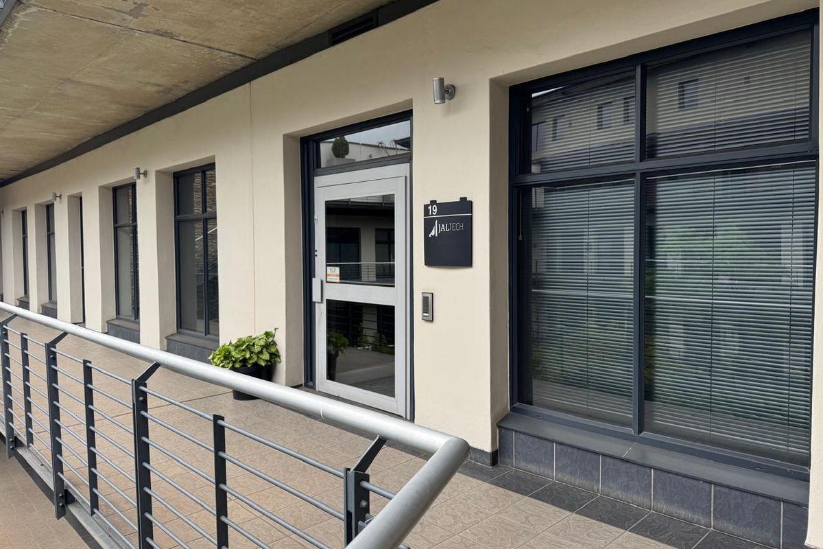 Professional office entrance featuring a modern aluminium-framed glass door, large windows with integrated blinds, and a tiled balcony with a secure metal balustrade.