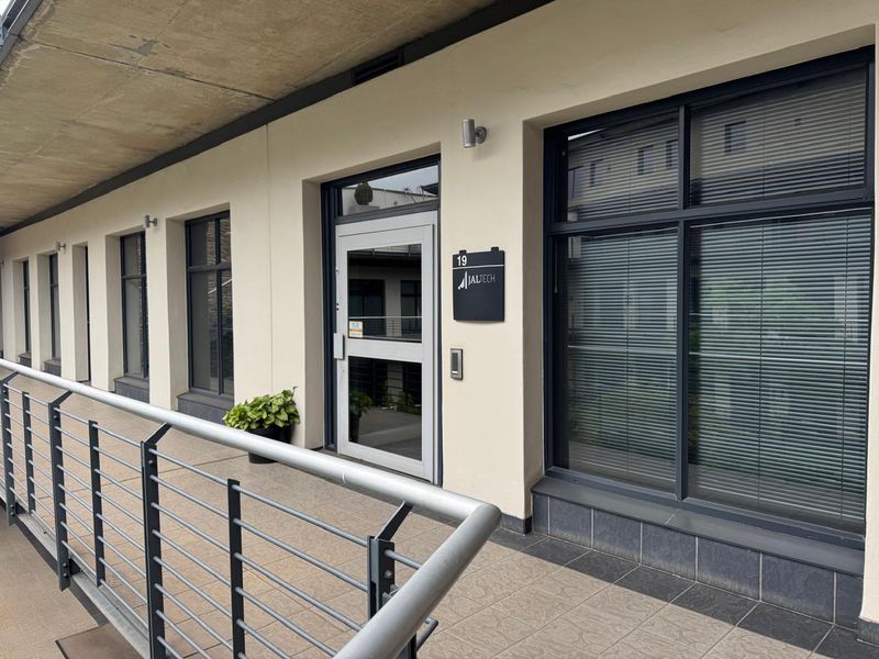 Professional office entrance featuring a modern aluminium-framed glass door, large windows with integrated blinds, and a tiled balcony with a secure metal balustrade.