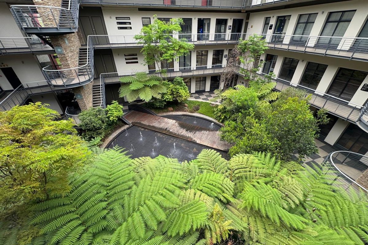 A well-maintained central courtyard featuring a water feature, wooden footbridge, and lush landscaping surrounded by multi-level office building walkways.