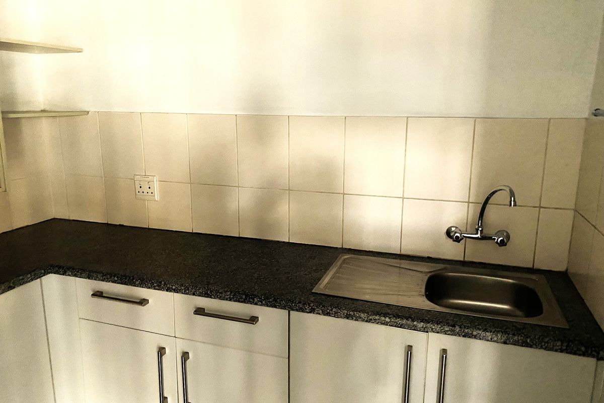 A functional kitchen area featuring white cabinetry, a dark granite-style countertop, a stainless steel sink with a chrome faucet, and tiled splashback.