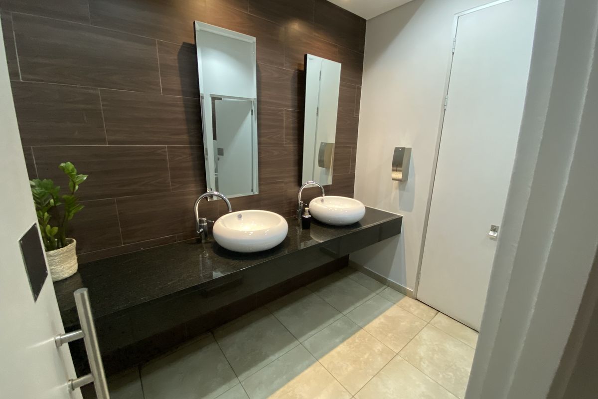 Modern office restroom featuring a floating granite vanity with dual vessel sinks, wood-look tiled feature wall, and contemporary fixtures.
