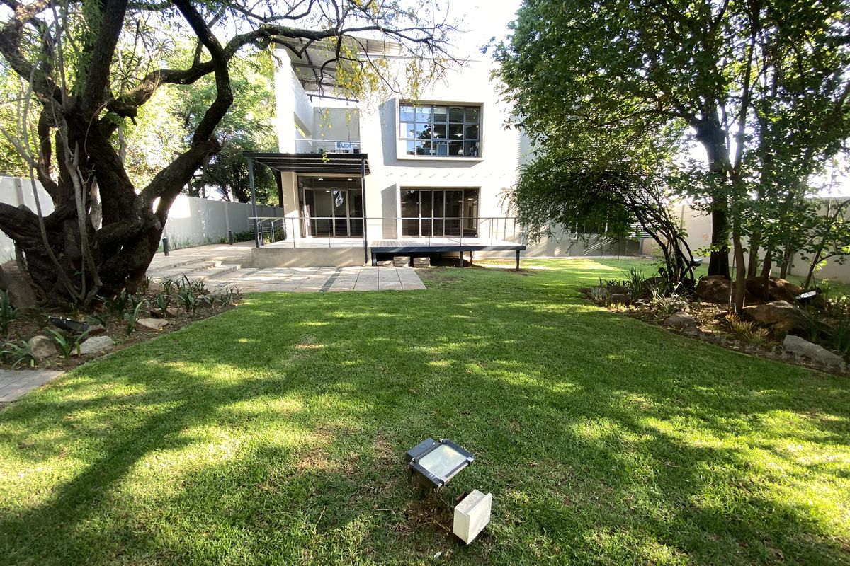 A view of the rear exterior of the office building, featuring a landscaped garden, paved patio area, and modern architectural facade with large windows.