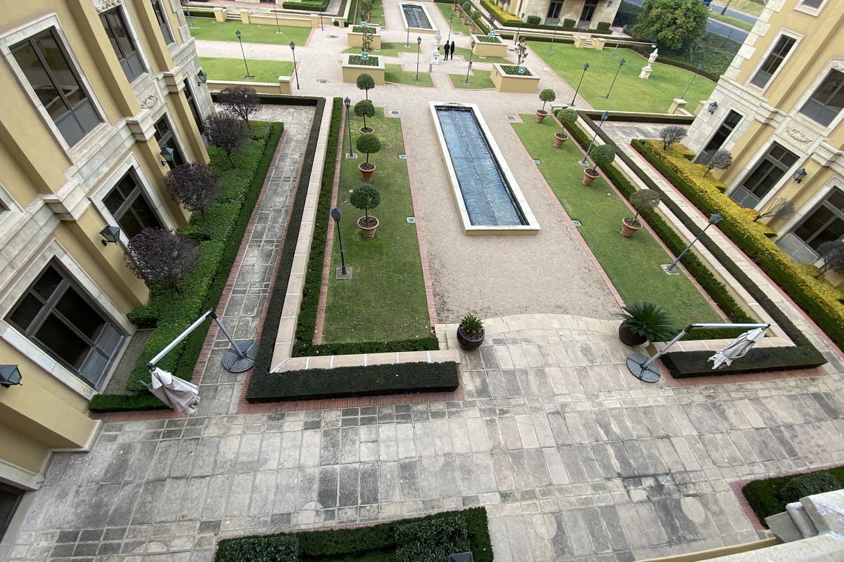 An elevated view of a well-maintained office complex courtyard featuring manicured lawns, structured hedges, a central water feature, and paved walkways.