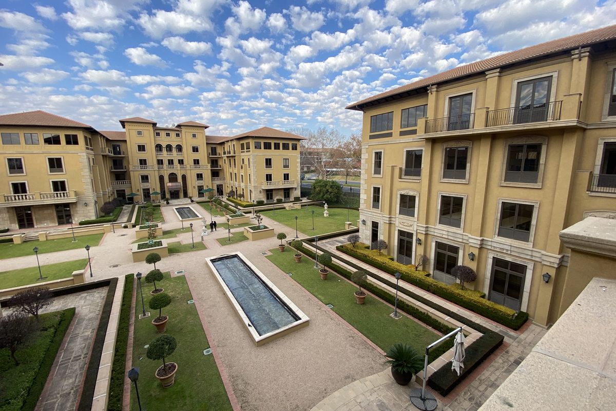 Elevated view of a well-maintained office complex courtyard featuring landscaped gardens, manicured lawns, paved walkways, and a central water feature.