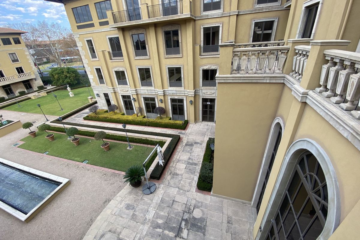 Elevated view of the office building courtyard featuring manicured gardens, stone paved walkways, a water feature, and classic architectural facade details.