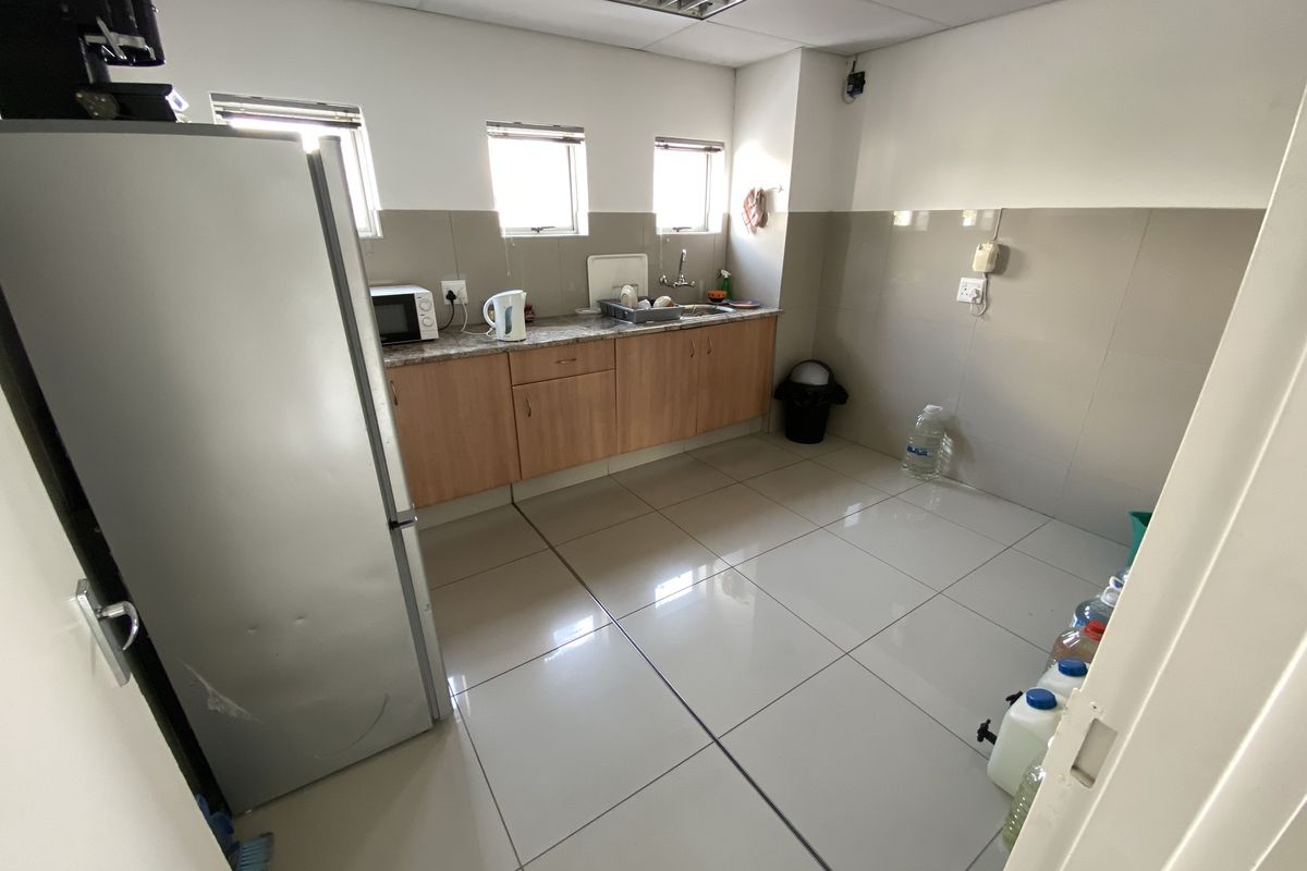 A functional industrial kitchenette featuring tiled flooring, laminate cabinetry, granite-look countertops, and a stainless steel sink with tiled splashbacks.