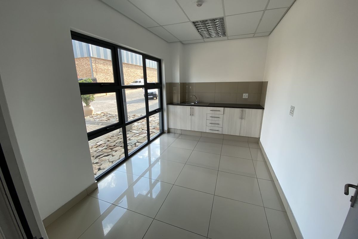 A clean, modern kitchenette area featuring tiled flooring, built-in cabinetry with a sink, and large windows providing natural light.